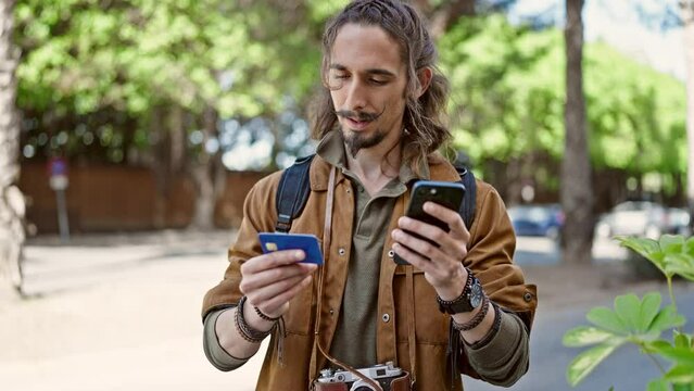 Young hispanic man tourist shopping with smartphone and credit card at park