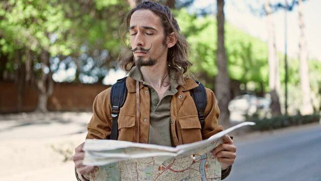 Young hispanic man tourist wearing backpack looking city map at park