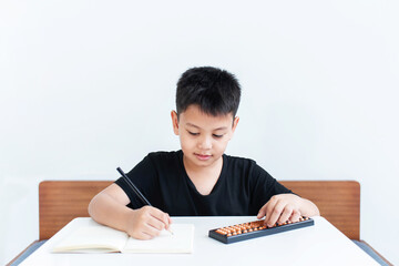 Asian boy in homeschooling, writing and using abacus for learning math, education concept, Social distancing, stay home, showcasing a modern, educational lifestyle