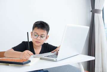 Little Asian boy student using computer laptop learning, virtual internet online class from school teacher. Homeschooling and education concept. Presenting a modern educational way of life.