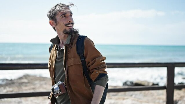 Young hispanic man tourist wearing backpack smiling at seaside