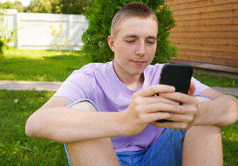 Portrait of a boy who sitting on the grass and looking in smartphone with a smile