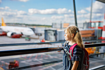 Little girl at the airport waiting for boarding at the big window. Cute kid stands at the window against the backdrop of airplanes. Looking forward to leaving for a family summer vacation