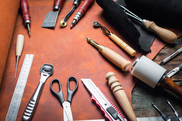 Leather pieces and leather craft work tools on the old wooden workbench background.