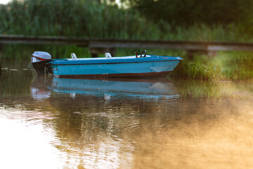 The blue boat on the lake at the calm, misty sunrise