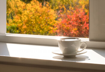 Cup of hot drink on the windowsill, autumn morning.
