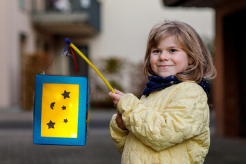 Little preschool kid girl holding selfmade traditional lanterns with candle for St. Martin...