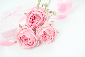 Three pink roses with ribbon and giftbox on the white table