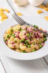 Piato di deliziosa pasta condita con cubetti di prosciutto cotto e pisellini, cibo italiano 