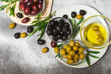 A set of green, red and black olives on a marble background. Various types of olives in bowls and fresh olive leaves. Vegan. Olive fruits. Place for text. Copy space.