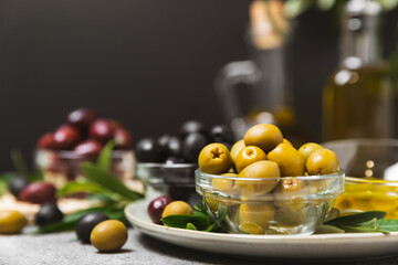 A set of green, red and black olives on a marble background. Various types of olives in bowls and fresh olive leaves. Vegan. Olive fruits. Place for text. Copy space.