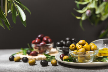 A set of green, red and black olives on a marble background. Various types of olives in bowls and fresh olive leaves. Vegan. Olive fruits. Place for text. Copy space.