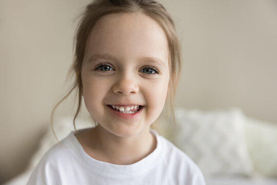 Happy adorable pretty preschooler girl with blue eyes and baby teeth looking at camera, smiling, posing at home. Close up facial portrait of little toddler kid enjoying childhood