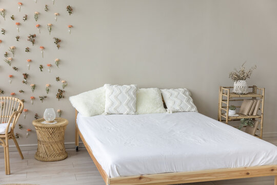 Wooden double bed with comfortable orthopedic mattress, white sheet, cushions in eco interior design. Stylish modern empty bedroom with no people, natural decoration, bamboo furniture