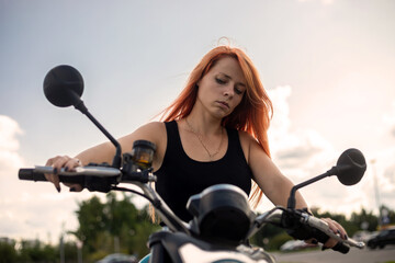 Fototapeta na wymiar Beautiful girl with red hair and a motorcycle. Big motorcycle. Girl on a motorcycle.