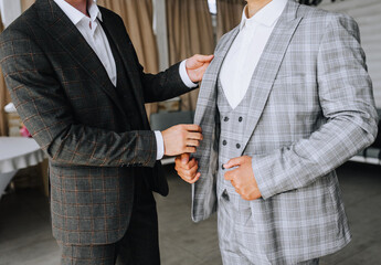 A friend of the groom helps the groom in a stylish gray suit in preparation for the wedding in the morning with clothes. Close-up photography, portrait.