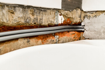 new polyethylene flexible plumbing pipes are routed into chiseled brick wall above white bathtub under removed ceramic tiles during installation of new water supply in bathroom