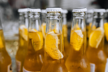 Open glass bottles with orange beer, an alcoholic cocktail with lemon inside stand in a row in a bar. Food photography.