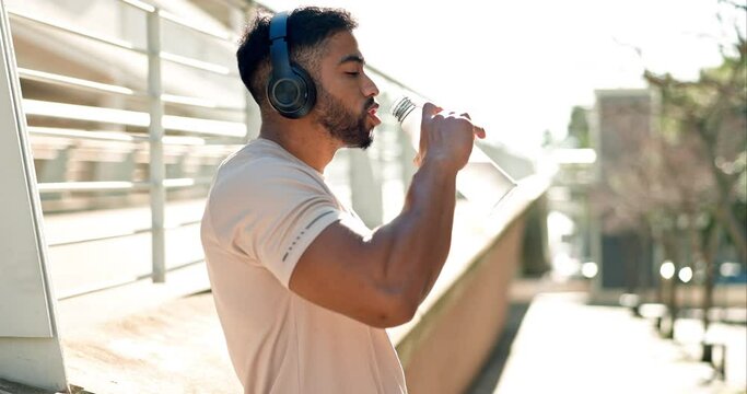 Sports, man and drinking water in city for fitness break, exercise and workout with headphones. Thirsty indian runner, bottle and hydration for energy, healthy recovery and listening to music outdoor