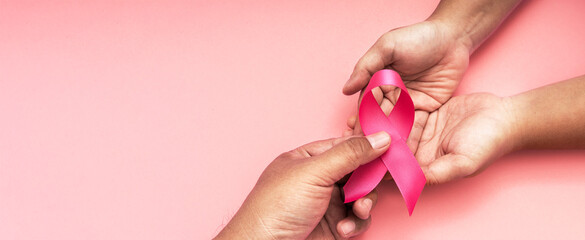 adult's hand giving a pink ribbon on the hand of a fat woman with cancer, world cancer day, healthcare and medicine backdrop, suicide prevention, children health care.