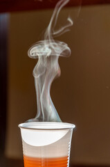 Particolare di fumo che esce da un bicchiere di plastica con del te dai toni caldi