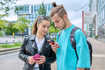 Teenage friends guy and girl standing together using smartphones