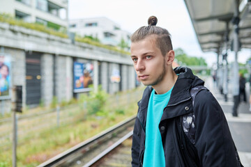 Young male waiting for an electric train at city railway station.