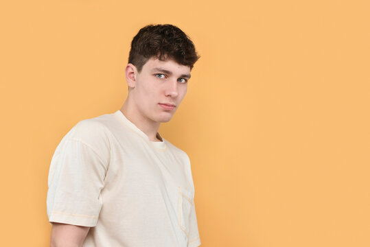 Young serious shy guy 18 years old on yellow background, copy space, advertisement. The boy has an inferiority complex, it is difficult for him to communicate with people