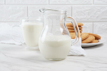 Milk in a transparent glass and jar on a marble table. Round ring shaped German spritz biscuits at background