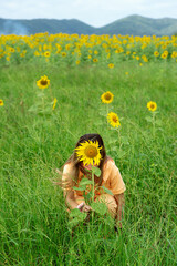 Asian woman hiding behind yellow and green sunflower