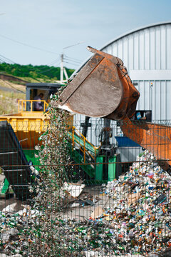 Pouring trash from excavator bucket on recycling plant yard