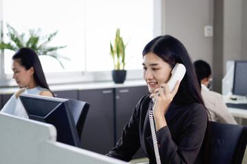Beautiful Asian woman operator officer talking with customer by using landline phone at working...