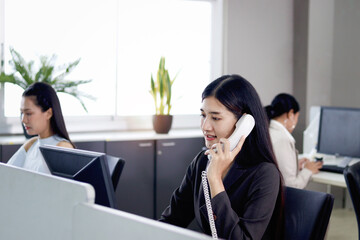 Beautiful Asian woman operator officer talking with customer by using landline phone at working...