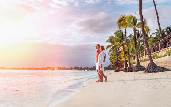 Couple in love hugging on sandy exotic beach while having evening walk by Trou-aux-Biches seashore on Mauritius island enjoying sunset. People relationship and tropic honeymoon vacations concept image