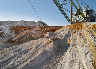 Bucket of walking excavator hangs over chalk pile and pond