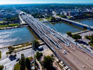 New triple tied-arc railroad bridge with four tracks, footbridge and bicycle lane over Vistula river in Krakow, Poland. Far view of new Krakow Zablocie railway station. Aerial view - 645705955