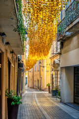 The streets of Beziers, in the Languedoc region of the South of France, are decorated for summer with overhanging decorations made of gold disks, that shine in the sunshine and blow in the wind
