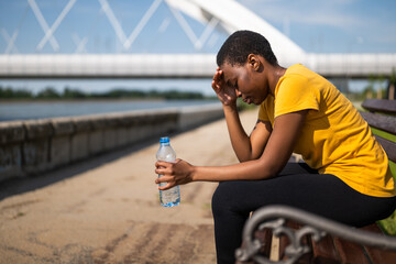 Exhausted woman after exercise drinking water while sitting on bench.	
