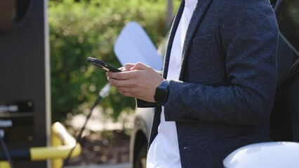 Businessman using smartphone and waiting power supply connect to electric vehicles for charging the battery in car. Plug charging an Electric car from charging station