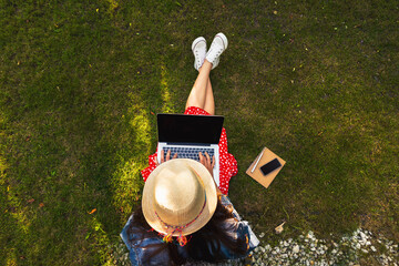 Top view of a young woman sitting on the grass with a laptop in her hands - 645729711