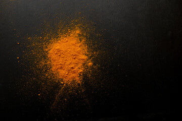 Fototapeta na wymiar Orange curry powder explosion on black texture, soft focus