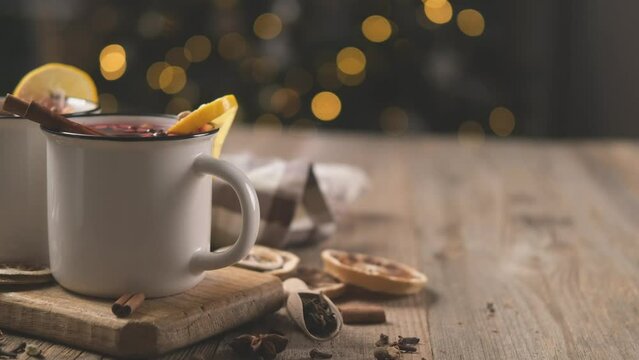 Mulled wine decorated with cinnamon and lemon in steel mugs standing on christmas illumination background