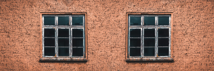 Fototapeta na wymiar zwei alte und verwitterte Fenster mit Sprossen im Ausschnitt einer Hausfasade als Hintergrund