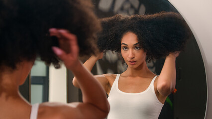 Young beautiful African American woman girl enter to bathroom looking pampering mirror reflection...