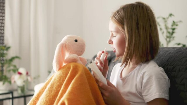 cute little girl using a cold spray to her runny nose, schoolgirl has a fever due to virus