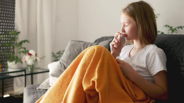 cute little girl using a cold spray to her nose, schoolgirl has a fever and runny nose due to virus