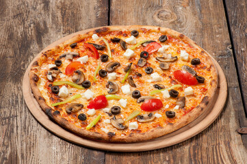 Studio shot of a hand made pizza with mushrooms, tomato, green peppers, olives and feta cheese on beautiful weathered wooden table