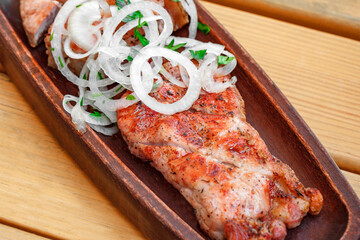 Grilled grilled meat with onions on wooden stand, selective focus