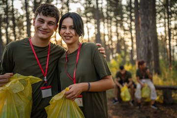 portrait couple in front of group of friends volunteers prepare to collect garbage waste and clean forest nature in summer day slow motion - obrazy, fototapety, plakaty