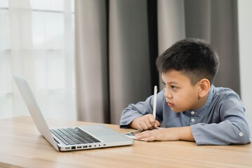 Fototapeta premium Little Asian boy student using computer laptop and tablet learning. Educational concept Social distancing, staying at home, presenting a modern educational way of life.